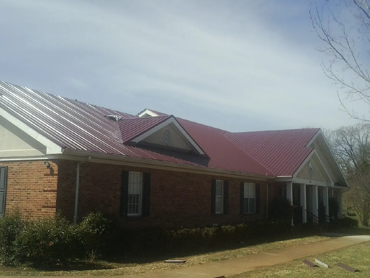 Red metal roof with gabled entries on a long brick building, from a Hail Damage Roof Repair job in Wingate