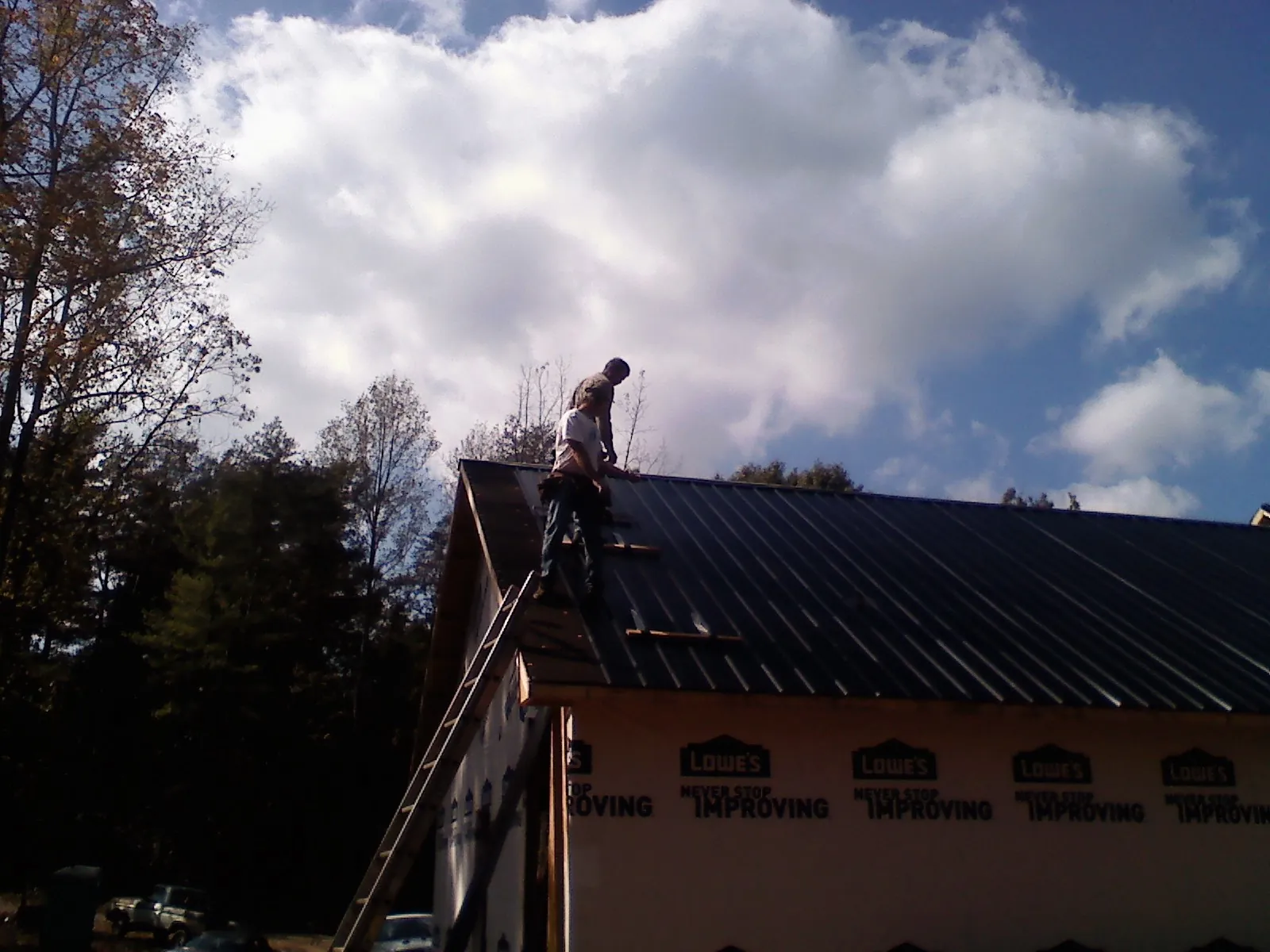 Roofer fastening dark metal panels high against a cloudy sky, from a Roof Inspection job in Wingate