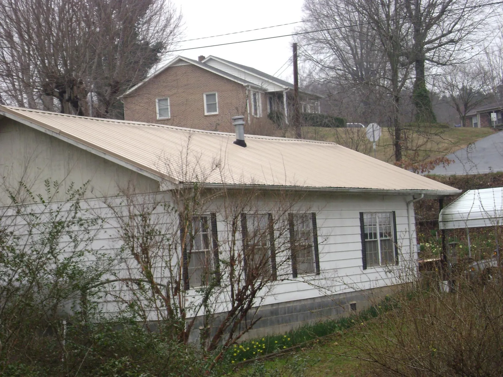 Tan metal roof on a white sided house set into a hillside — Commercial Roofing by Roofing Brothers in Wingate