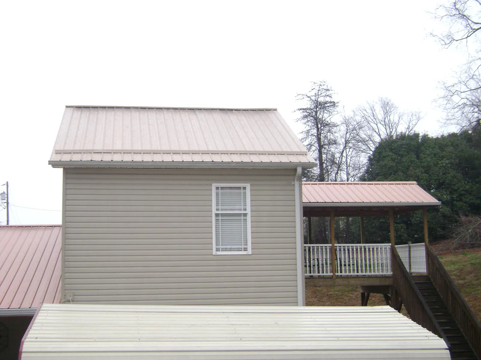 Tan metal roofs on a two story addition and attached porch, from a Roof Replacement job in Wingate